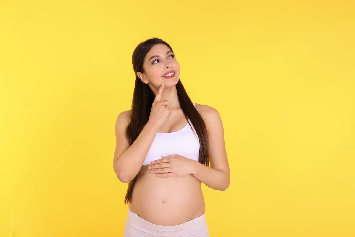 Mulher grávida pensativa sobre o bebê, sorrindo com um dedo no queixo