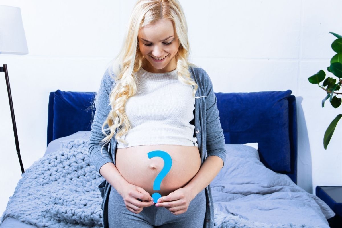 Mulher grávida em um quarto, segurando um ponto de exclamação na frente de sua barriga