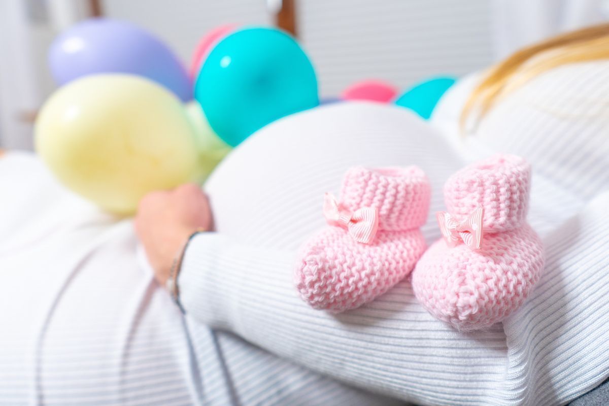 Mulher grávida com balões de festa coloridos e sapatinhos de bebê