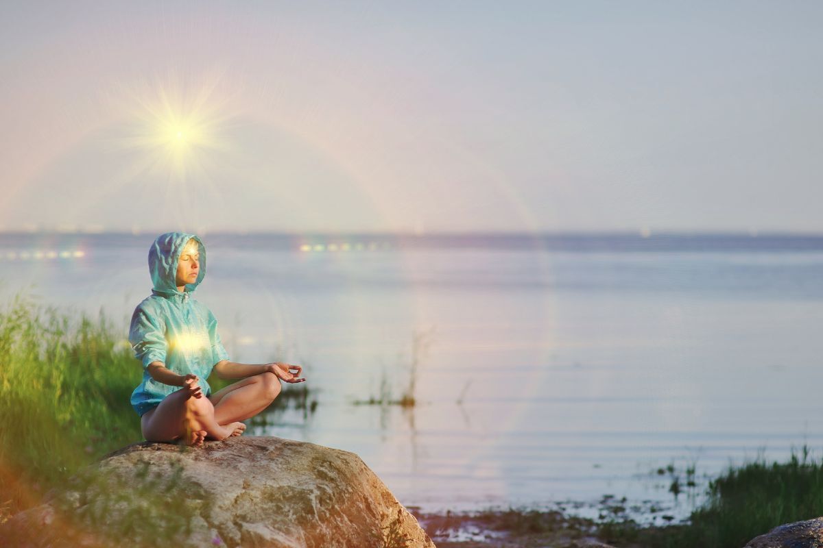 Mulher senta-se em uma pose de meio lótus praticando meditação de Yoga, mar e céu azul de verão, chakra brilhante, olhos fechados, calma.