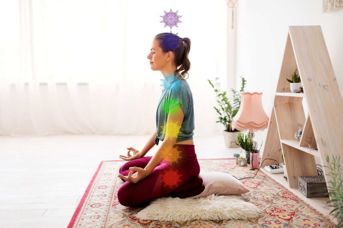 Mulher meditando na posição de lótus na sala de Yoga com sete símbolos de chakra destacados de acordo com cada cor representada