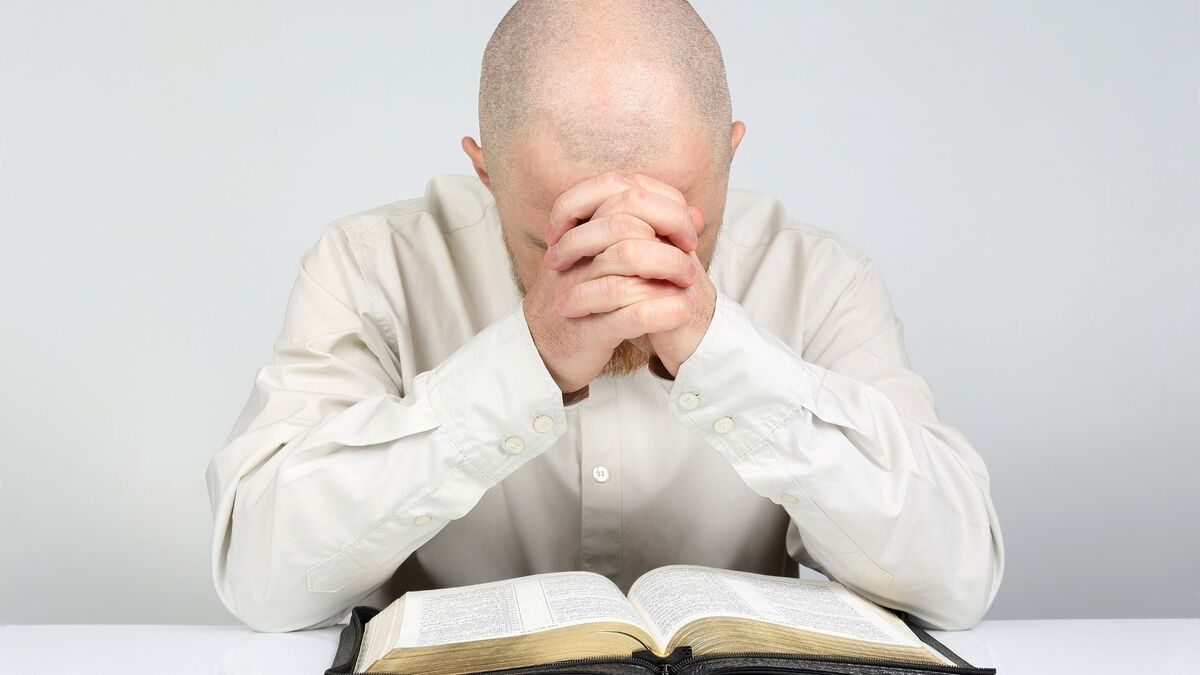 Homem orando com uma bíblia.
