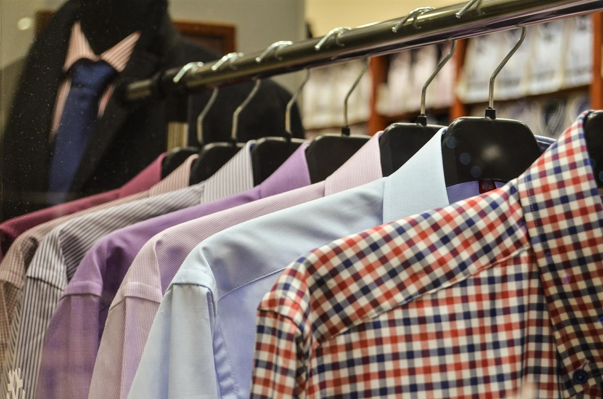Camisas de diversas cores e tipos enfileiradas em arara de roupas. 
