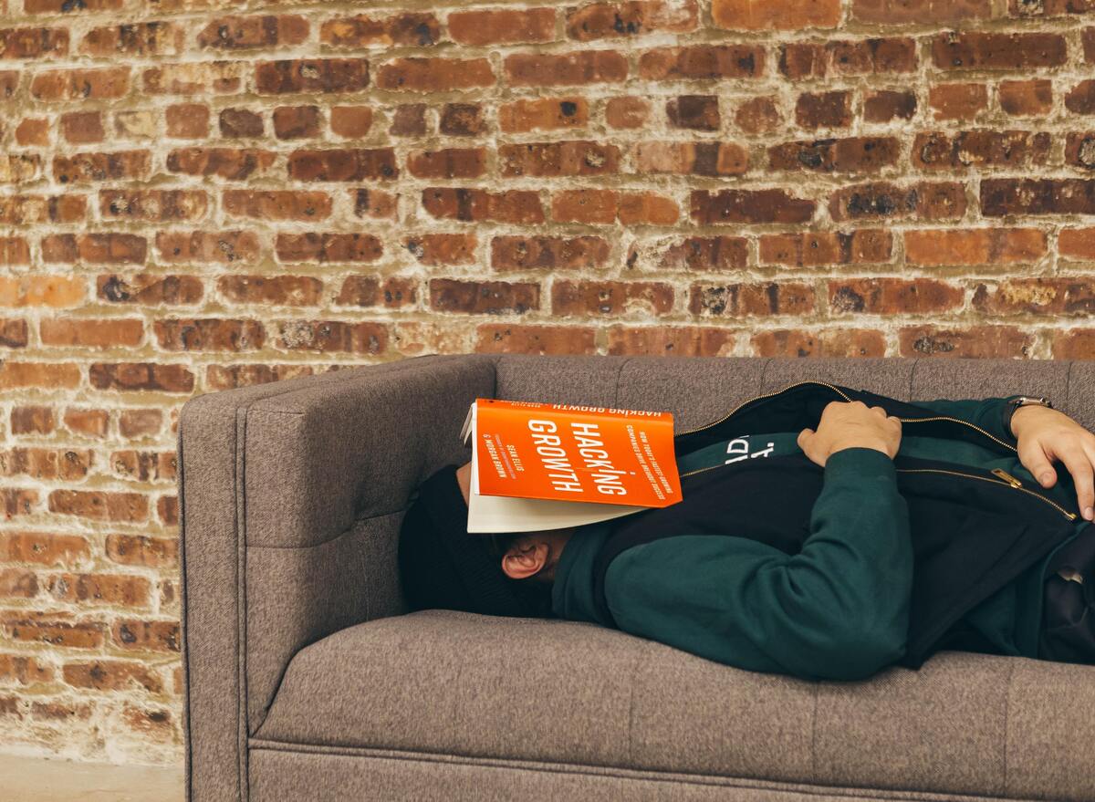 Homem dormindo no sofá com um livro no rosto.