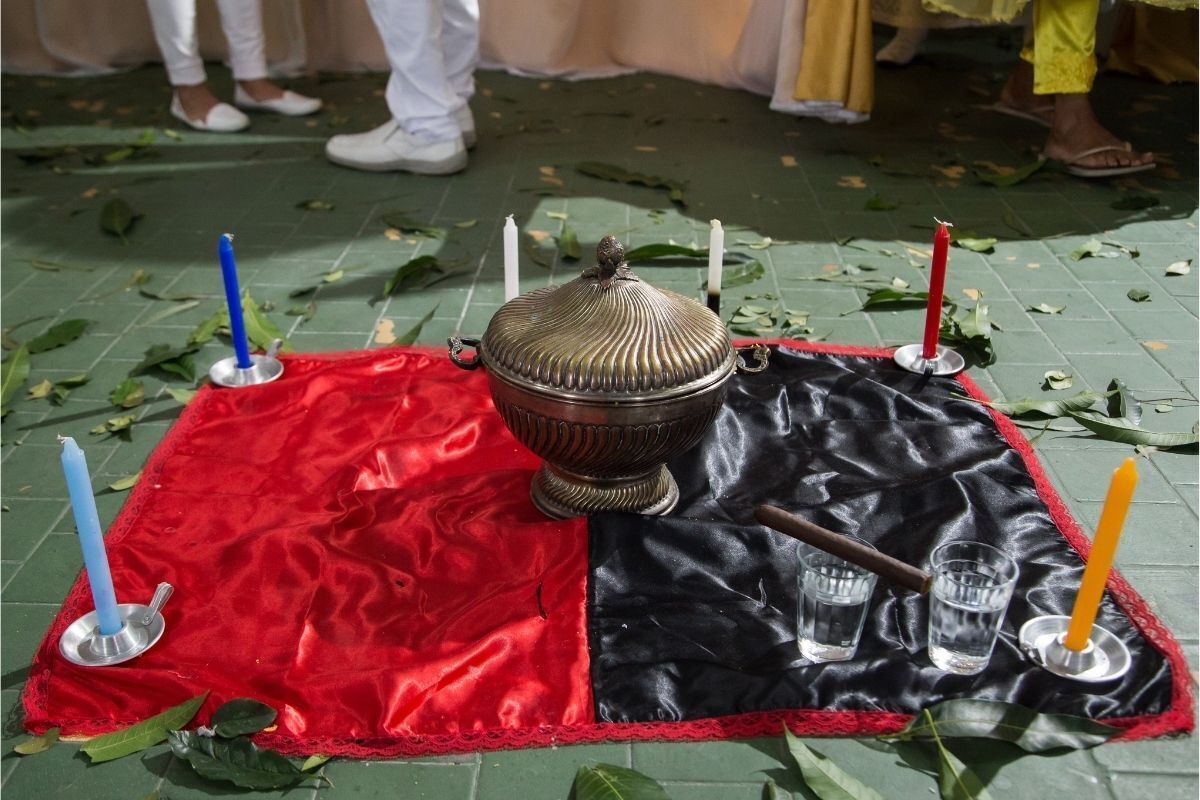 Ritual de Umbanda com uma quartinha rodeada de velas coloridas em um tapete vermelho e preto de seda