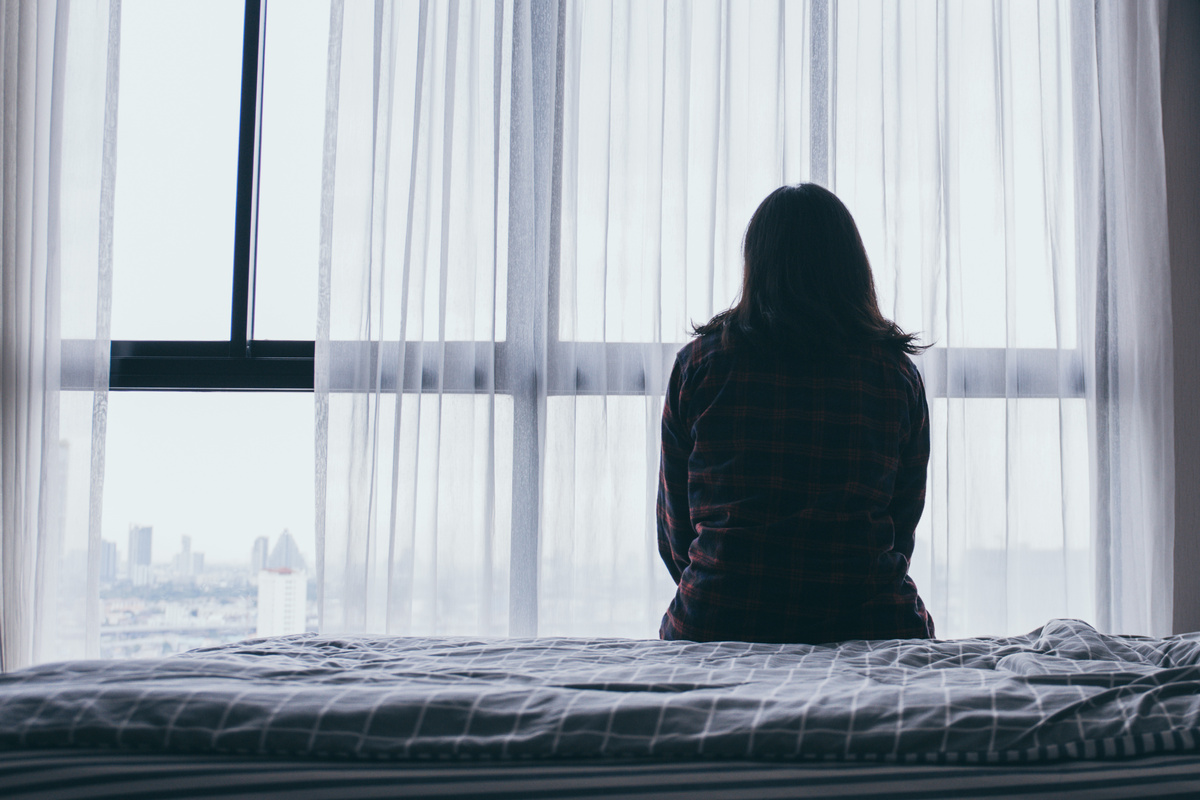 Mulher deprimida sentada na cama olhando pela janela