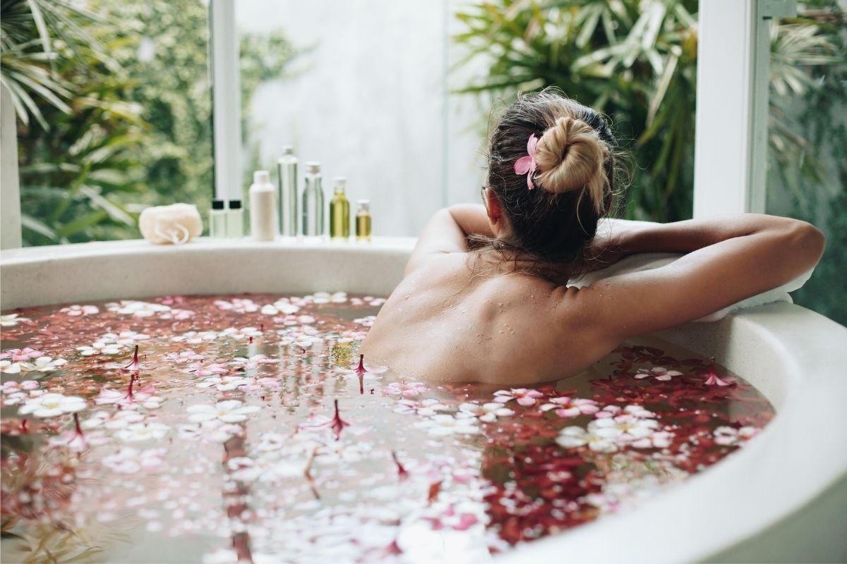 Mulher tomando banho de rosas, sentada de costas em uma banheira