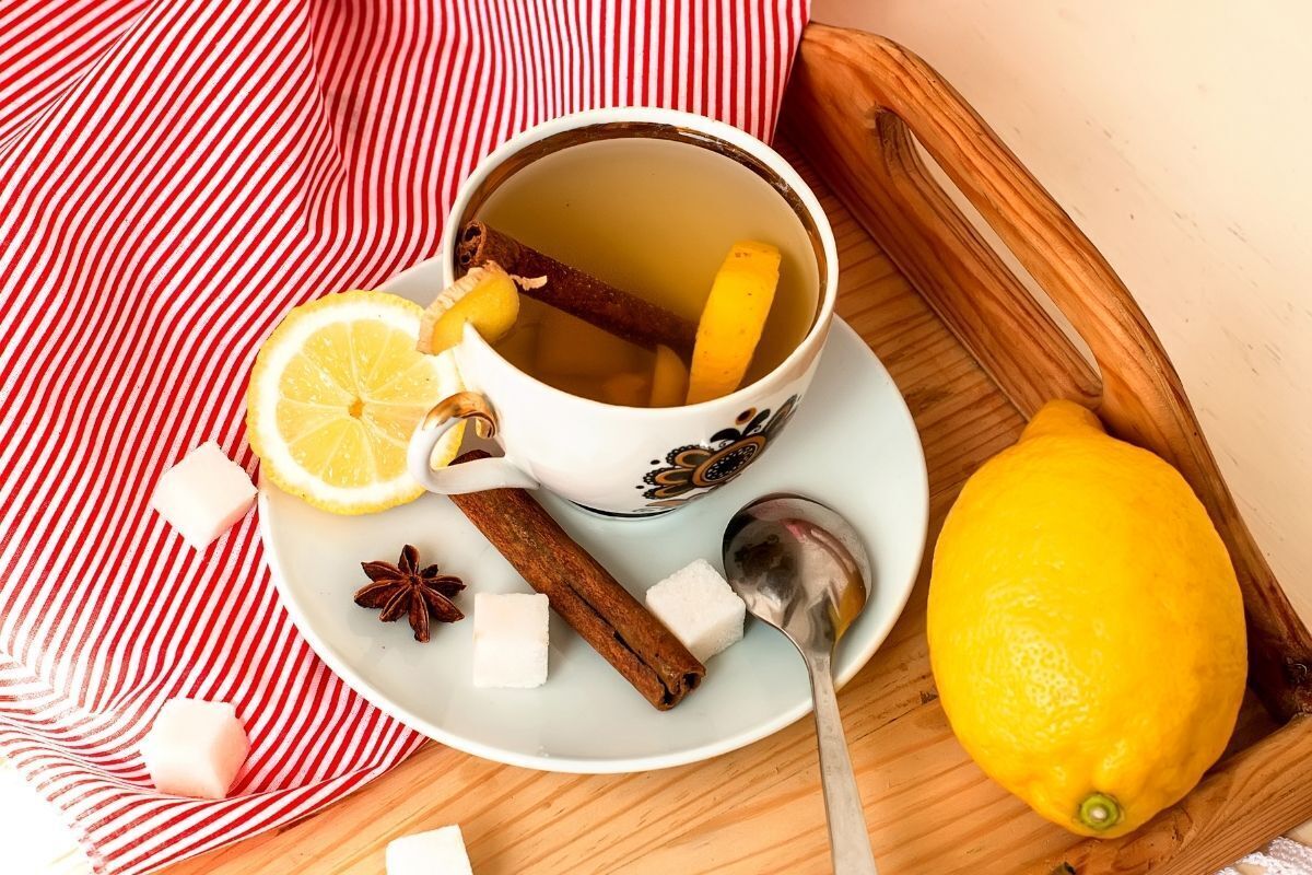 Chá de gengibre com canela e limão em uma xícara e pires brancos. Na mesa para servir café na cama, um guardanapo branco com listras vermelhas.
