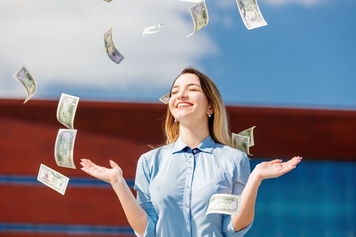 Mulher sorrindo com as mãos para o alto em uma chuva de dinheiro