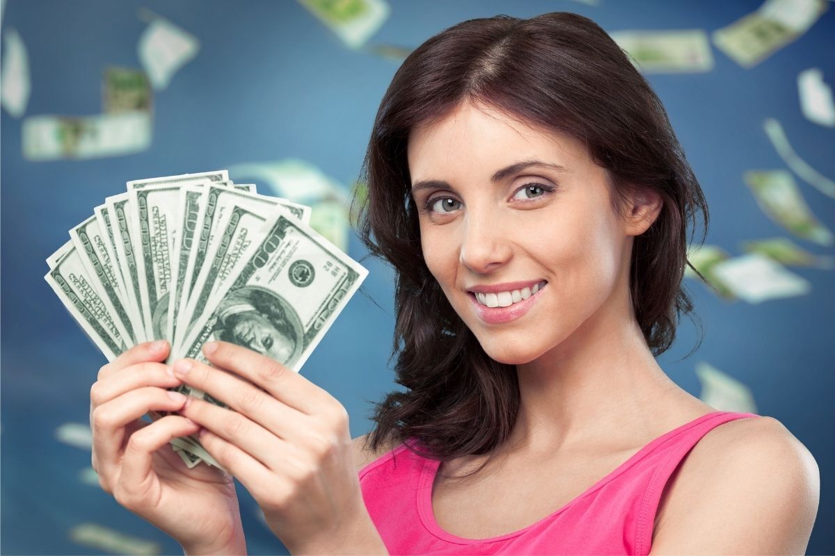 Mulher sorrindo segurando notas de dólar em suas mãos