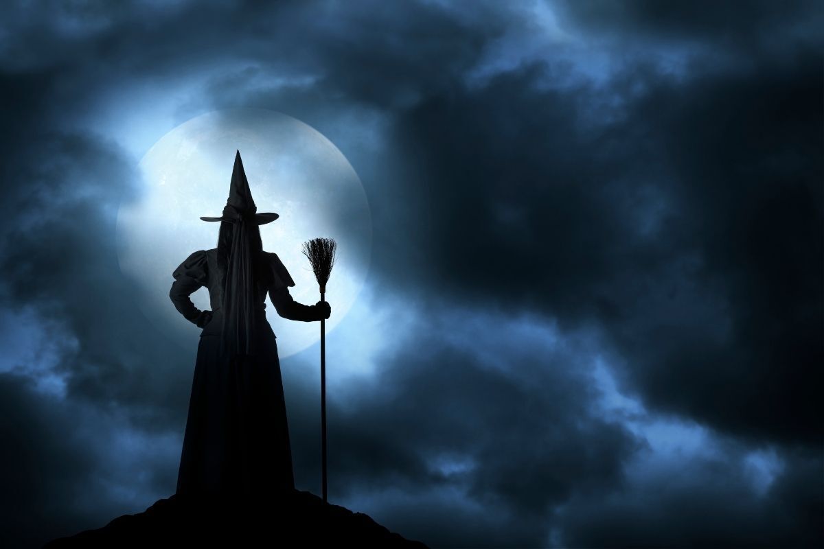 Ilustração da sillhueta de uma bruxa com chapéu e vassoura, Lua Cheia no fundo da imagem