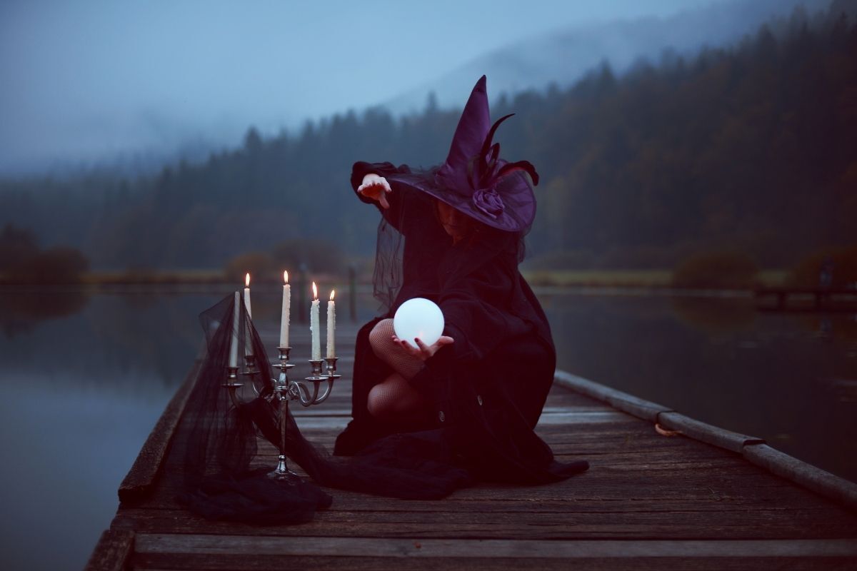 Velas bracas e uma bruxa vestida de preto, com uma bola de cristal em suas mãos