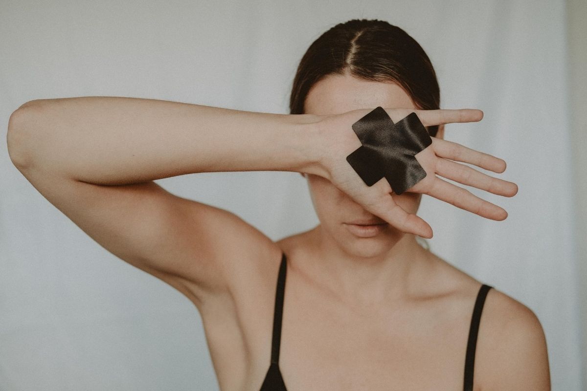 Fotografia representando o bloqueio emocional, mulher escondendo o rosto com a mão. Acima da mão, um X indicando traumas e bloqueios