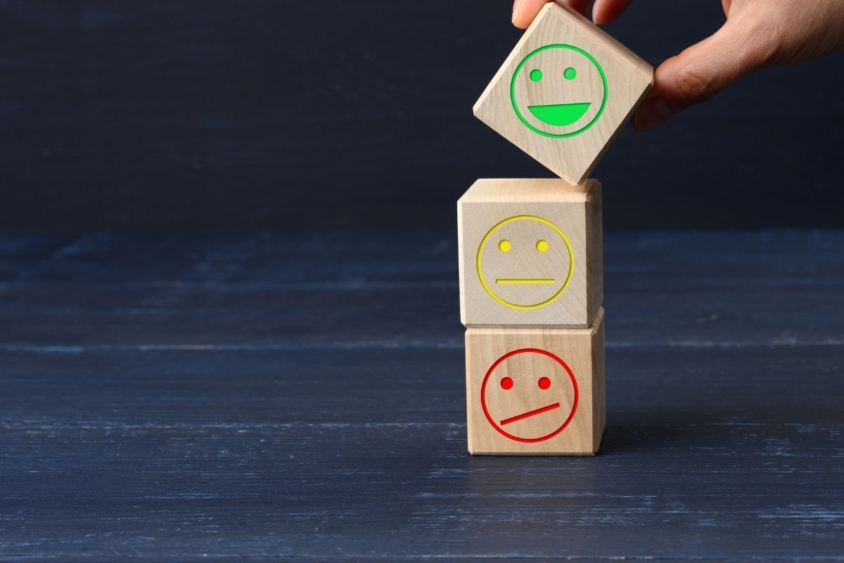 Imagem ilustrativa. Caixinhas de madeira com emojis simbolizando o bom humor, a decepção e a tristeza