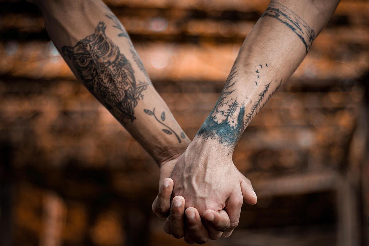 Duas pessoas de mãos dadas, ambas com os braços tatuados.