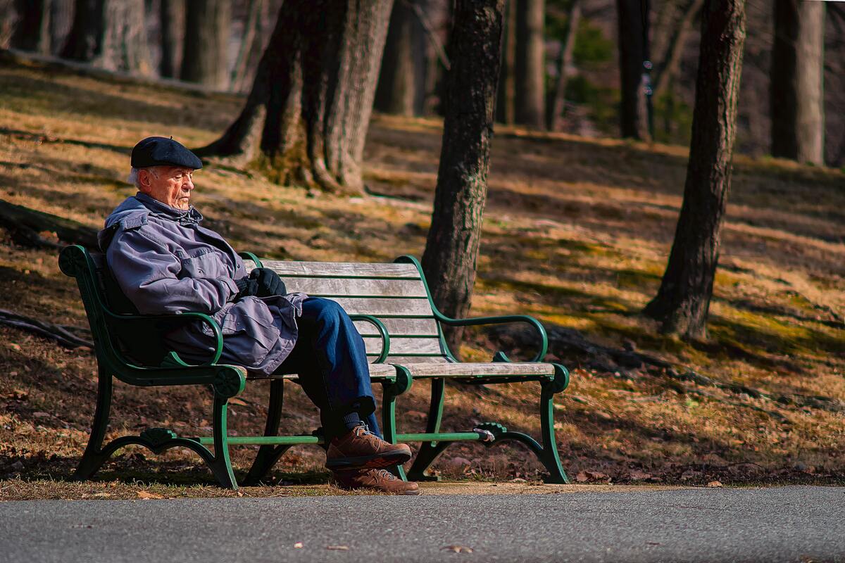 Homem idoso sentado em um banco de praça.