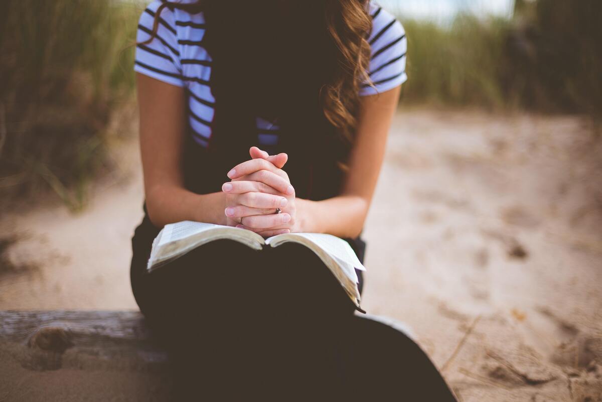 Mulher rezando em cima de uma bíblia. 