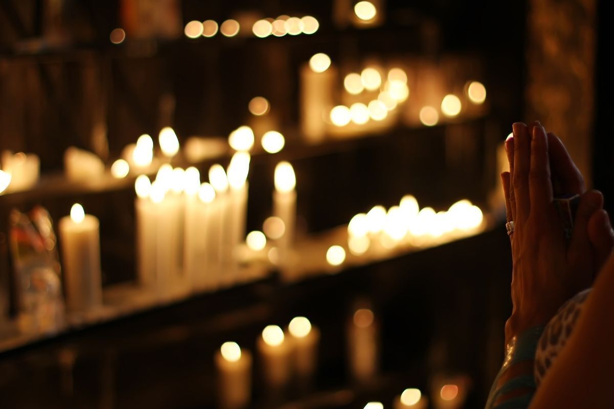  O sentido da vida e eternidade para as religiões. Na foto, uma pessoa orando em um ambiente repleto de velas acesas.