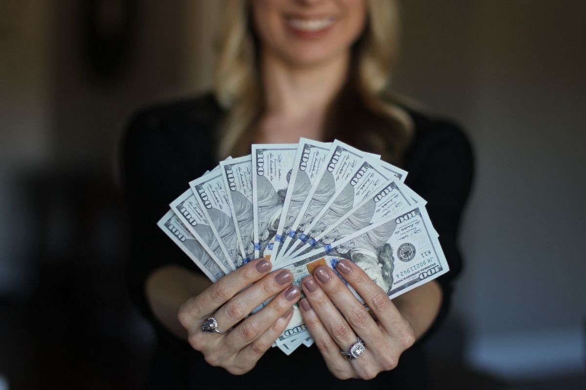 Mulher sorridente segurando notas de dinheiro nas mãos em formato de um leque