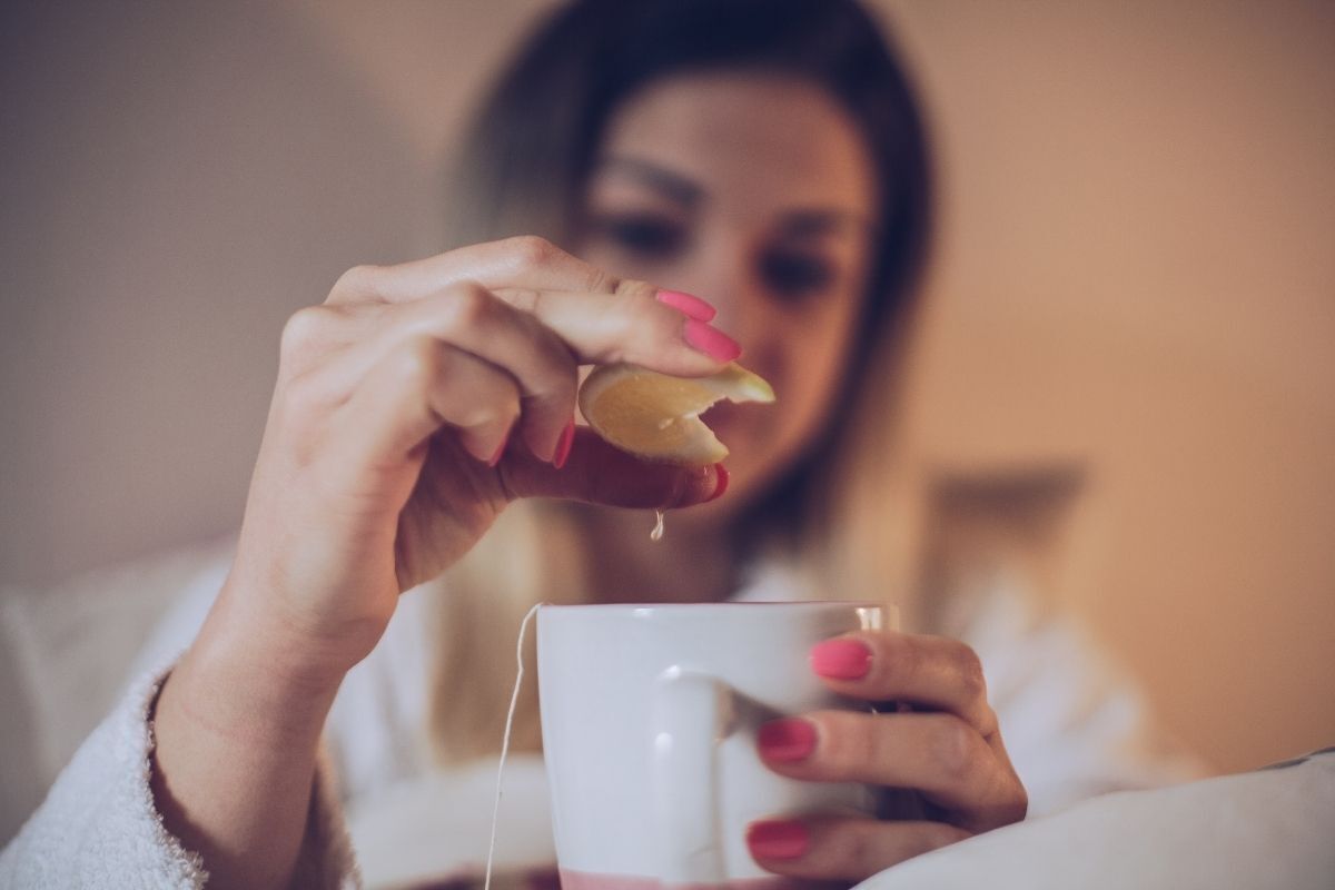 Mulher espremendo o limão em uma xícara de chá