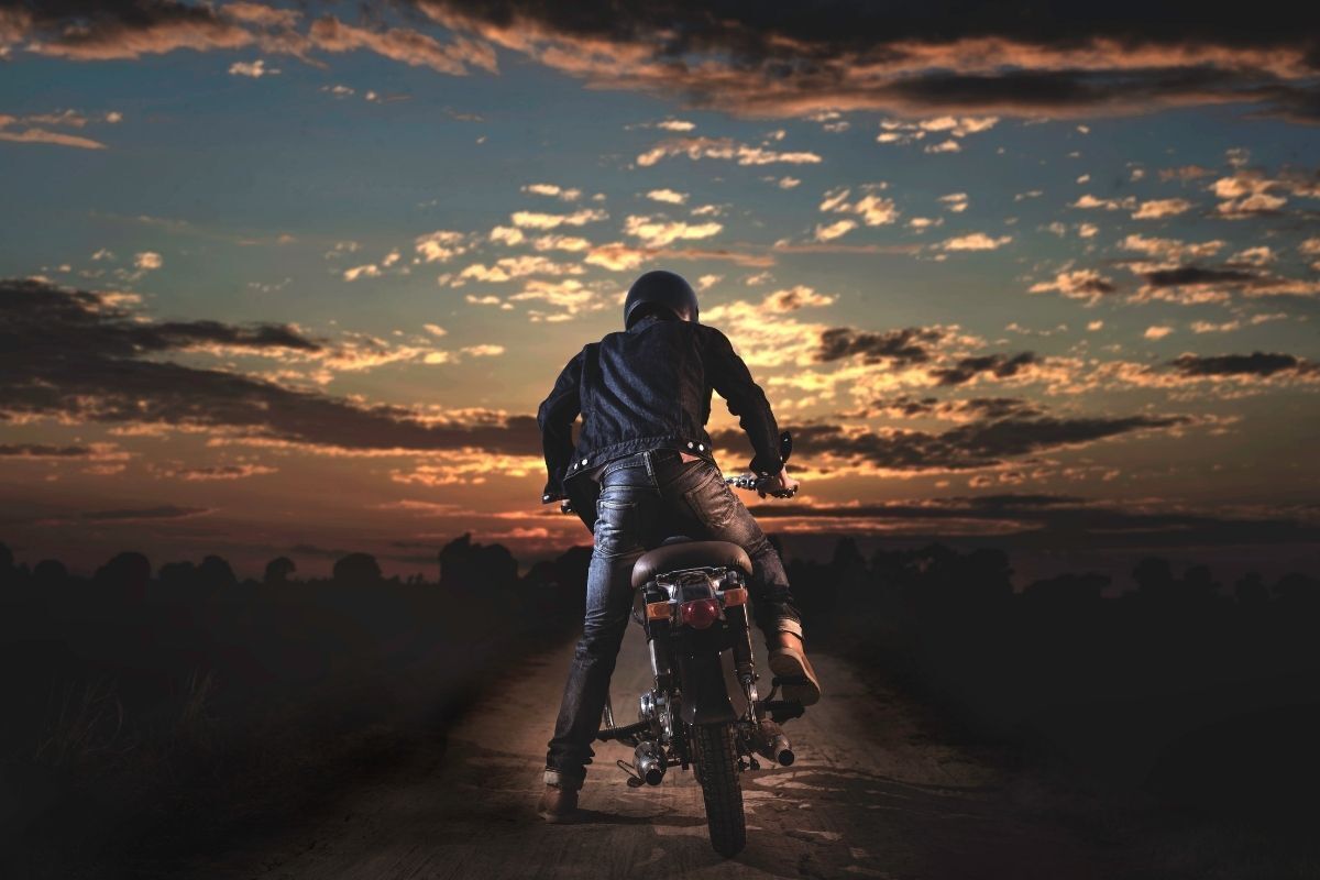 Motociclista dando partida em uma moto, em destaque o pôr do sol