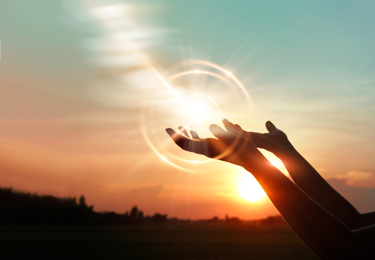 Mãos erguidas em sinal de oração com luz do sol refletida