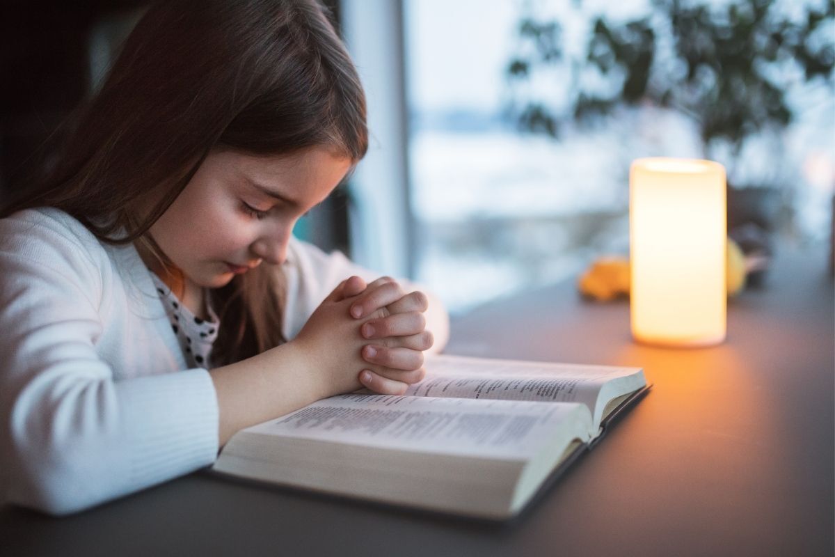 Criança rezando sob a bíblia