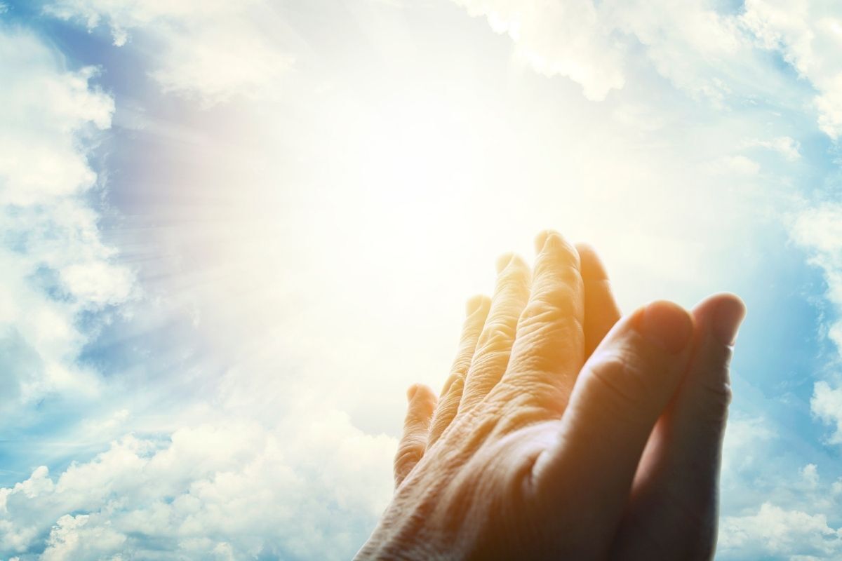 Ilustração de uma oração, com as mãos de uma pessoa direcionadas ao céu azul
