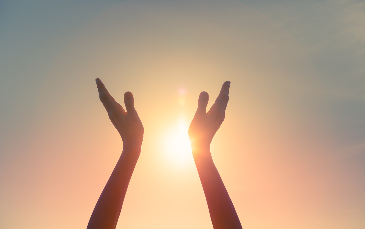 Mãos na direção do sol em sinal de oração