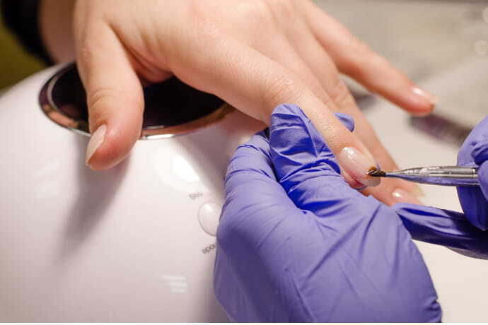Manicure de luvas de borracha aplicando base em unhas