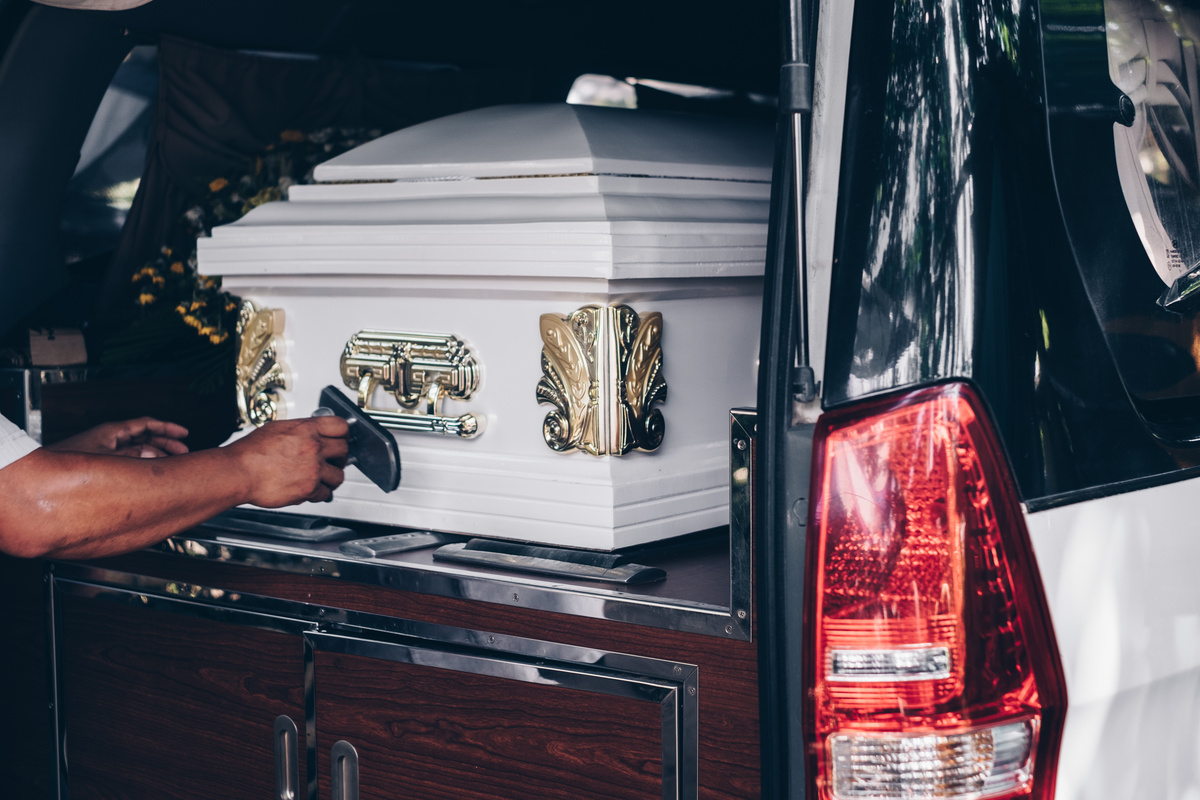 Pessoa retirando caixão de carro de funerária