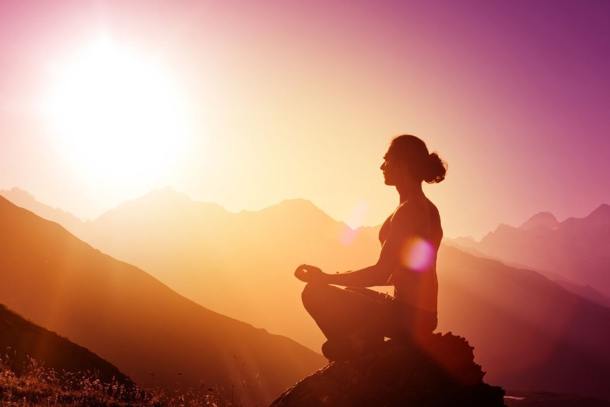Silhueta de uma mulher meditando nas montanhas no pôr do sol