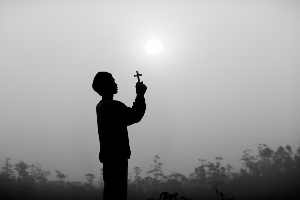 Silhueta de uma pessoa segurando uma cruz em suas mãos