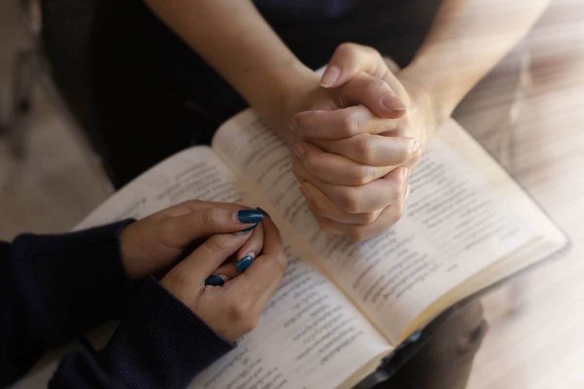 Mulheres rezando com as mãos na Bíblia Sagrada