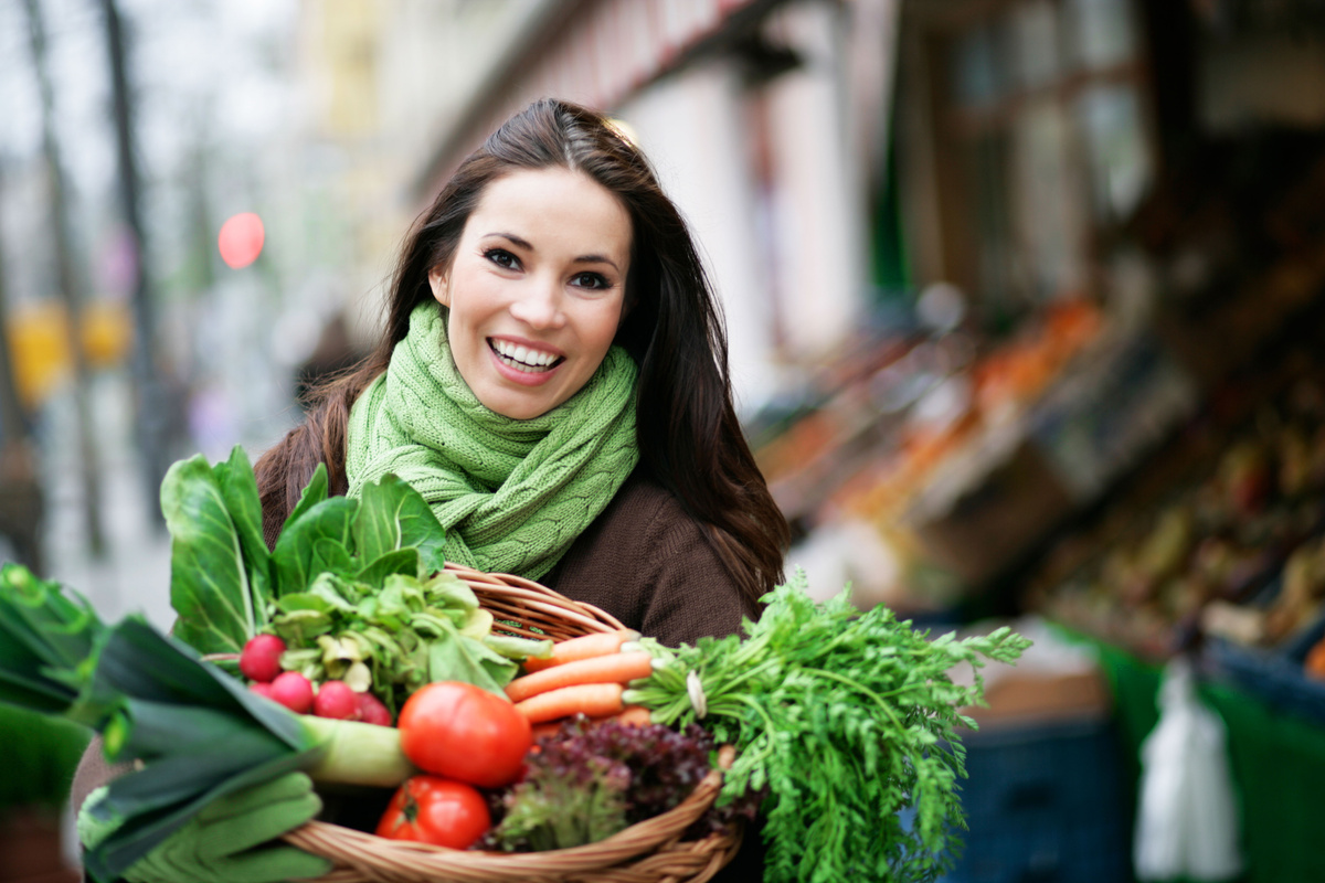 Mulher com cesta de compras cheia de vegetais.
