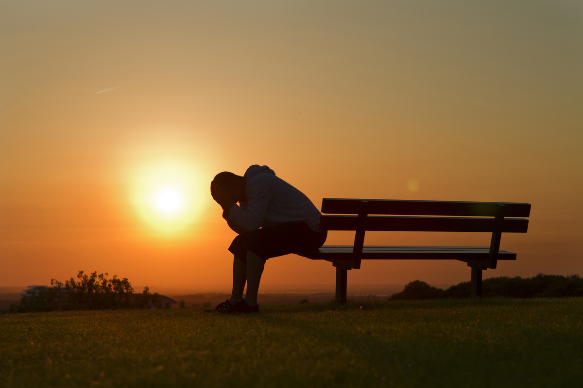 Pessoa triste sentada em banco no pôr do sol