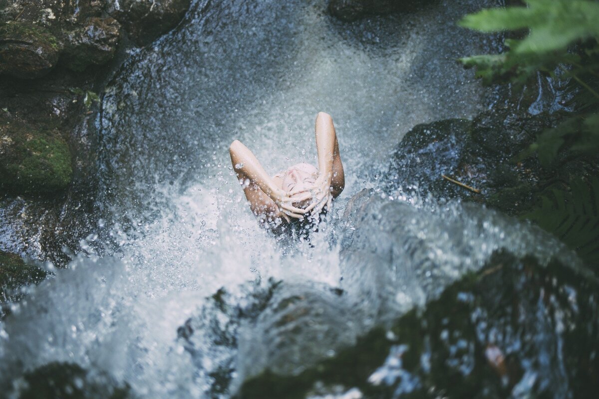 Vista de cima de mulher tomando banho de cachoeira.