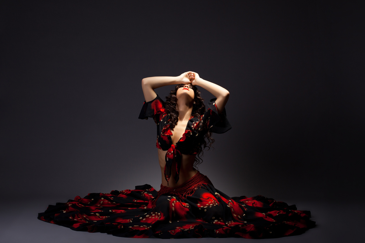Mulher com vestido vermelho e preto sentada em ambiente escuro