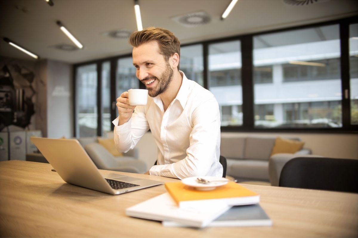 Homem feliz tomando café enquanto trabalha no laptop