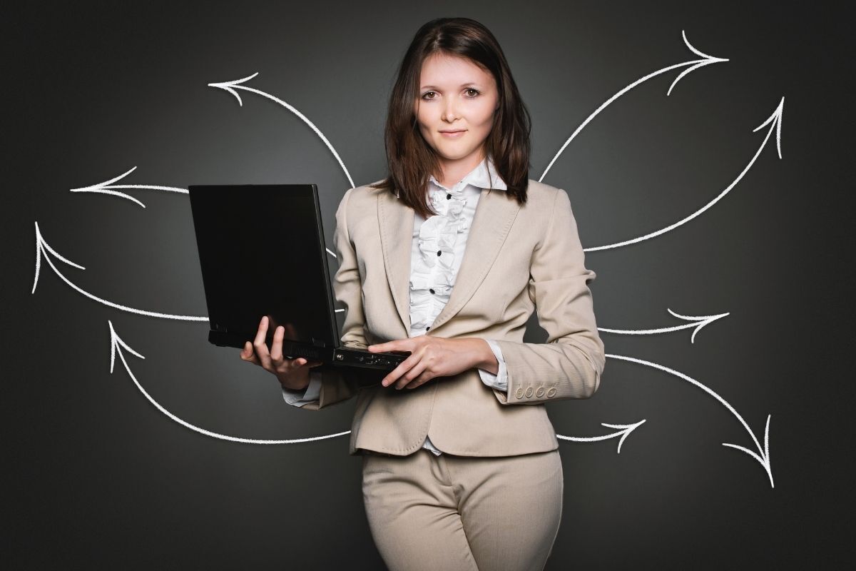 Imagem ilustrativa de uma mulher segurando um laptop com olhar confiante. No fundo há várias flechas, indicando diversas opções