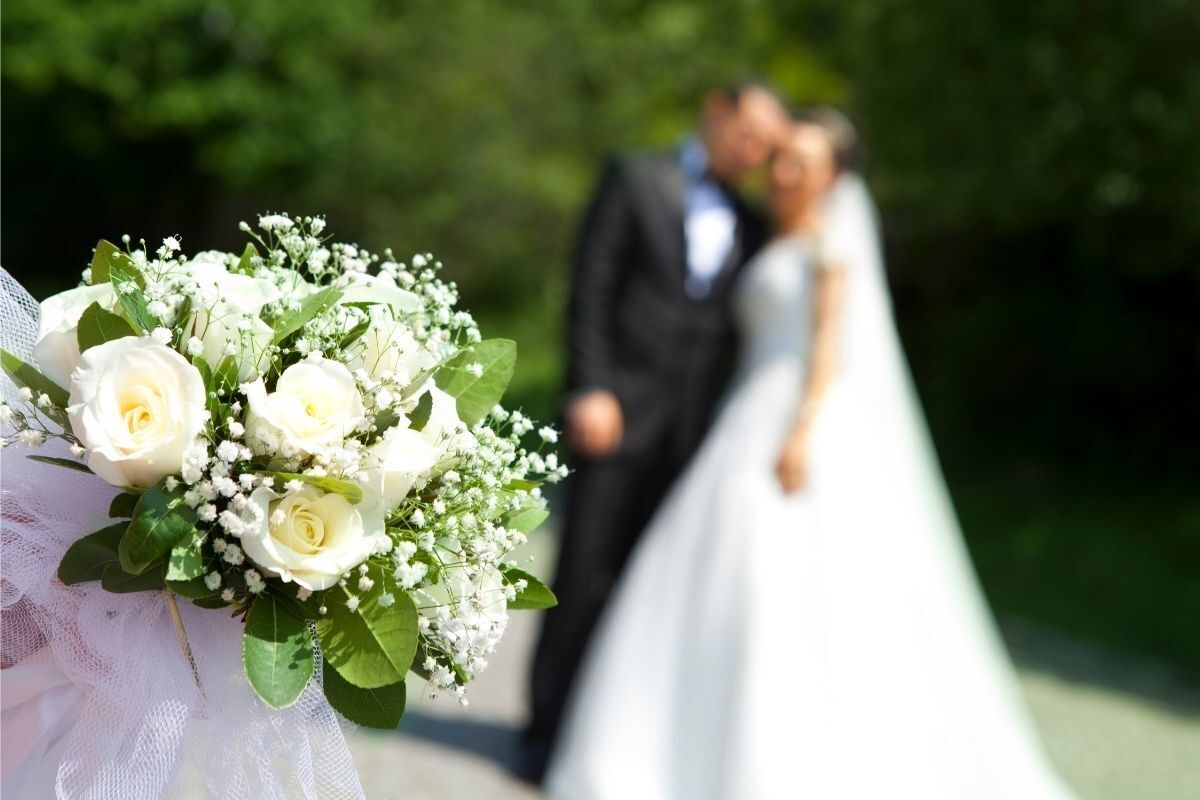 Flores brancas em um casamento. Ao fundo, em desfoque, um casal de noivos