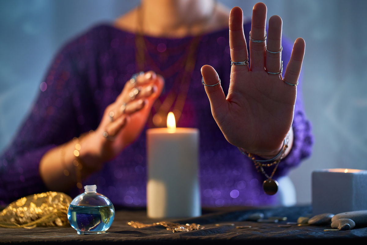 Mulher médium com a mão para frente, sentada em frente a mesa com vela