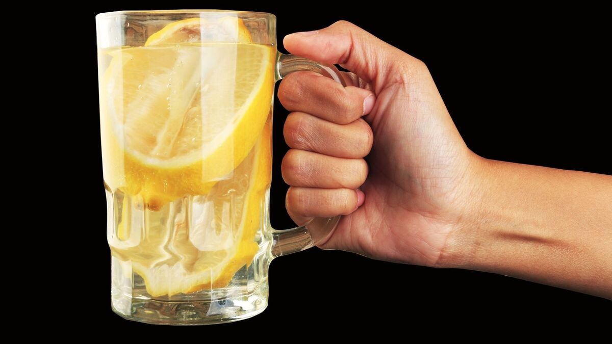 Mão segurando uma caneca de água com limão.