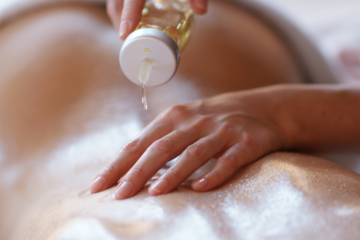 Mãos femininas colocando óleo no corpo de pessoa durante massagem tântrica
