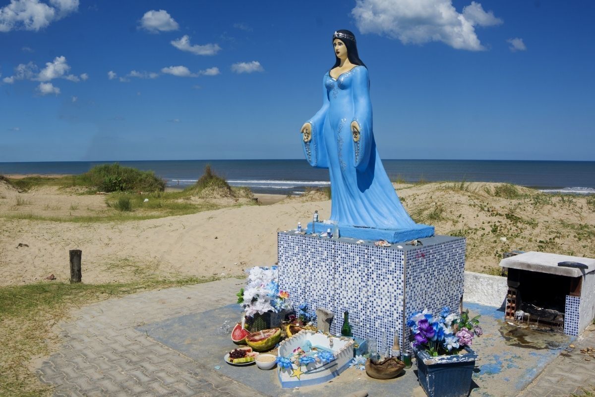 Estátua grande de Iemanjá na praia com oferendas 