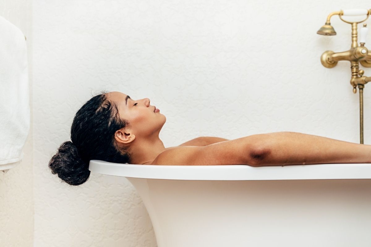Mulher tomando banho em uma banheira, relaxada com os olhos fechados