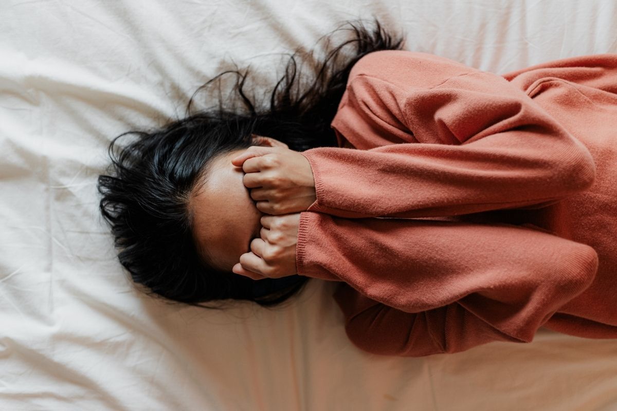 Mulher deitada na cama, com suas mãos fechadas cobrindo os seus olhos