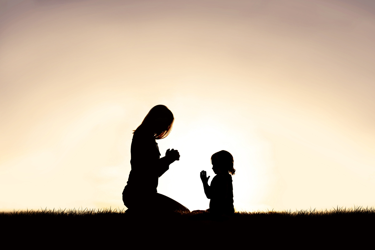 Mãe e filha rezando no pôr do sol