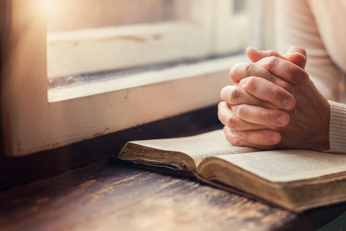 Mulher rezando com mãos na Bíblia