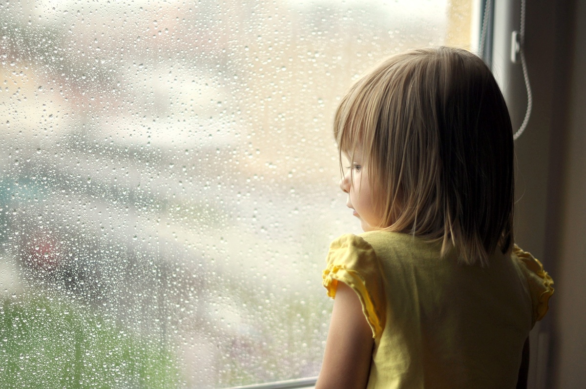 Criança olhando pela janela em dia chuvoso